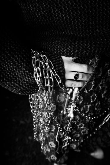 Hand adorned with a ring and hanging chains over a patterned fabric.