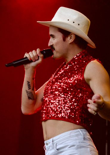 Singer in white hat and red sequin top performing with microphone.