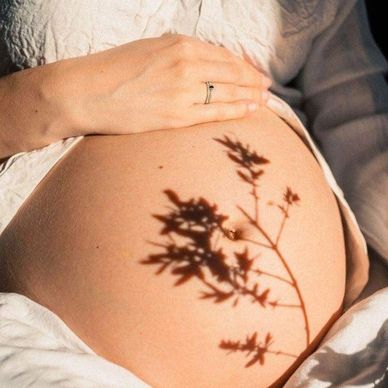 Shadow of a plant on a pregnant belly with a hand resting gently.