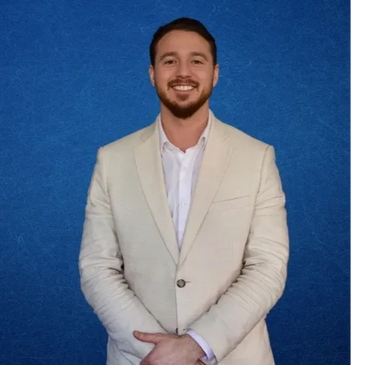 Smiling man in a beige suit jacket against a blue background.
