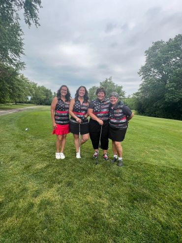 Four women posing on a golf course wearing matching jerseys.