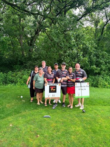 Group photo of eight people on a golf course holding signs.