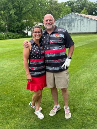 Couple in matching patriotic golf attire on a golf course.