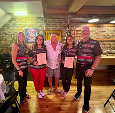 Group of five people posing indoors, two holding certificates.