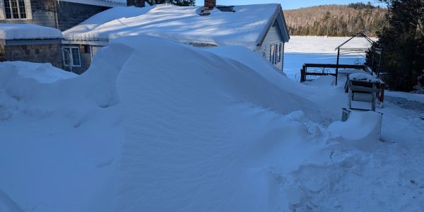 Car buried under heavy snow outside a house.