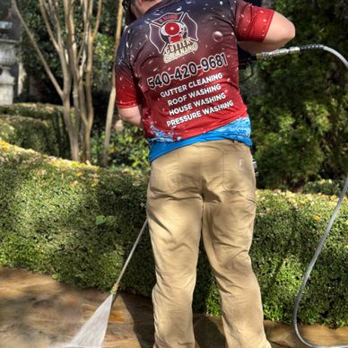 Worker power washing a patio, wearing a branded company shirt.