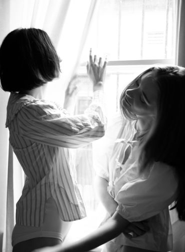 Two women interacting near a bright window.