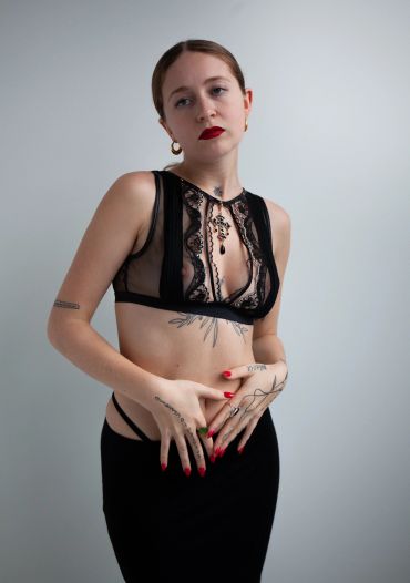 Woman in black lace top and skirt posing against a plain background.