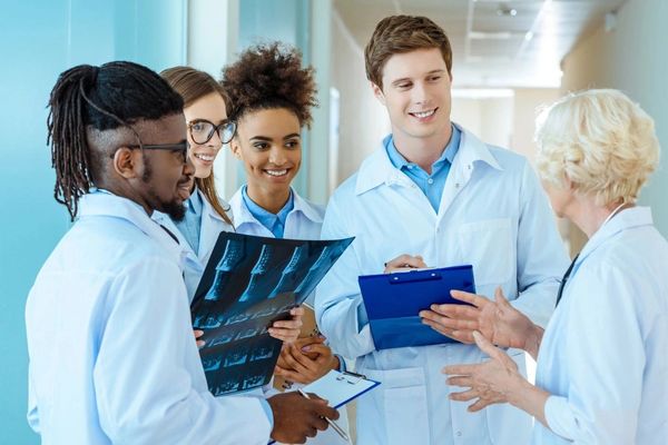 A multiracial group of young medical interns listening to a elder doctor in a hospital corridor