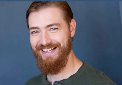 Smiling man with a red beard and blue eyes against a blue background.