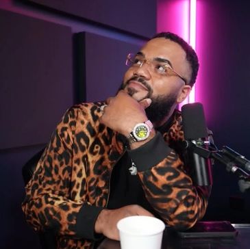 Man in leopard print jacket posing thoughtfully in front of a microphone with neon lighting.