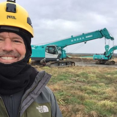 Man in yellow helmet at construction site with machinery.