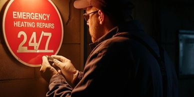 Technician inspecting tools near an emergency heating repairs sign at night.