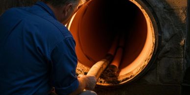 Man inspecting a large illuminated pipe or tunnel opening.