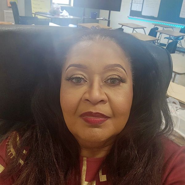 A woman with styled hair and makeup in a classroom setting.