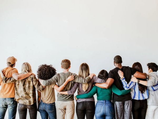 Diverse group of friends standing arm-in-arm facing a white wall.