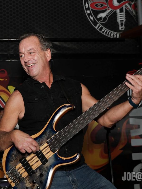 Man joyfully playing an electric bass guitar on stage.