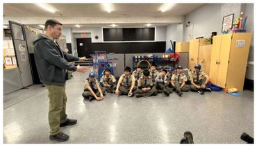 Leader instructs a group of scouts sitting on the floor in a classroom.