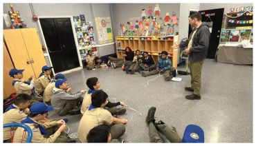 A group of scouts listening to a leader in a classroom setting.