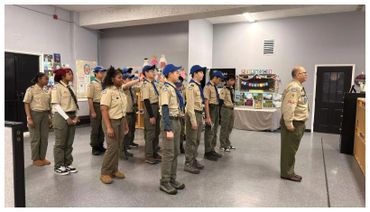 A group of scouts standing in formation indoors facing a leader.