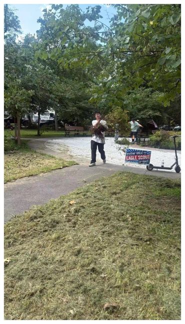 Man cleaning leaves in a park with an Eagle Scout sign nearby.