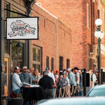 People waiting outside a restaurant called Cowboy Bar.