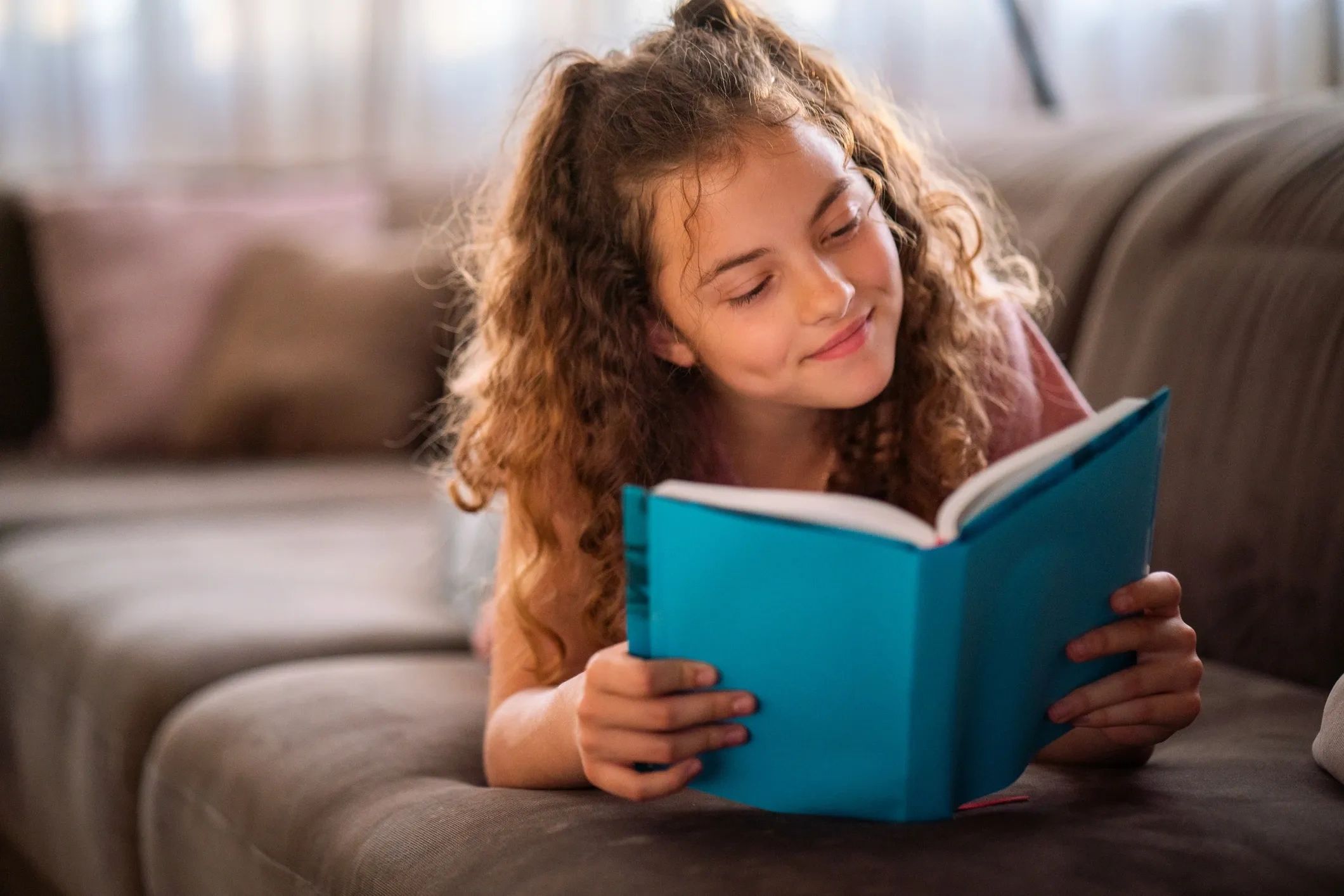 Girl reading a blue book on a couch.
