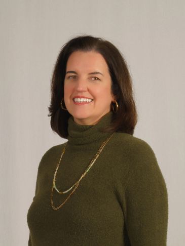 Smiling woman in green turtleneck sweater with gold jewelry.