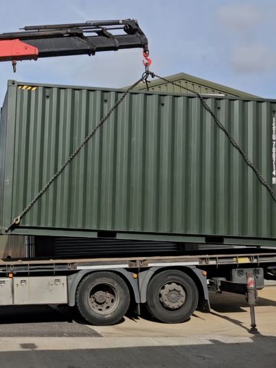 Green shipping container being lifted by crane on truck.