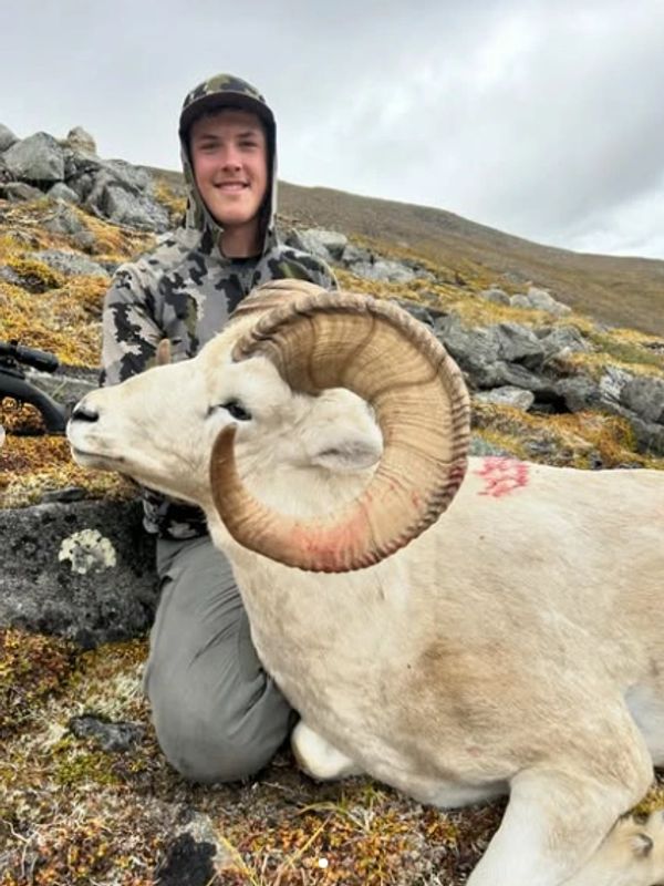 Young man in camouflage with a large ram on rocky terrain.