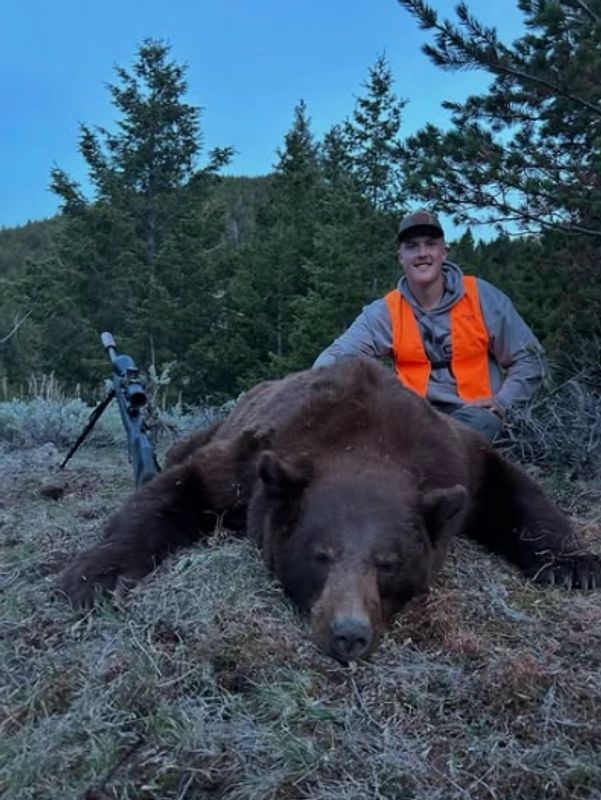 Hunter posing with a large bear he hunted in the forest.