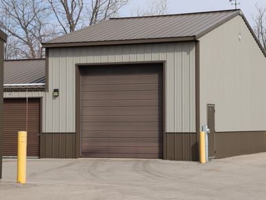 Metal building with a large brown garage door and beige siding.