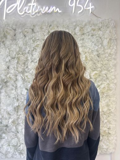 Long wavy blonde hair styled beautifully against a white floral backdrop.