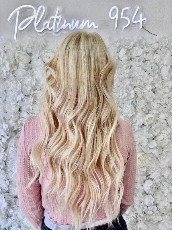 Long, wavy platinum blonde hair against a white floral backdrop.