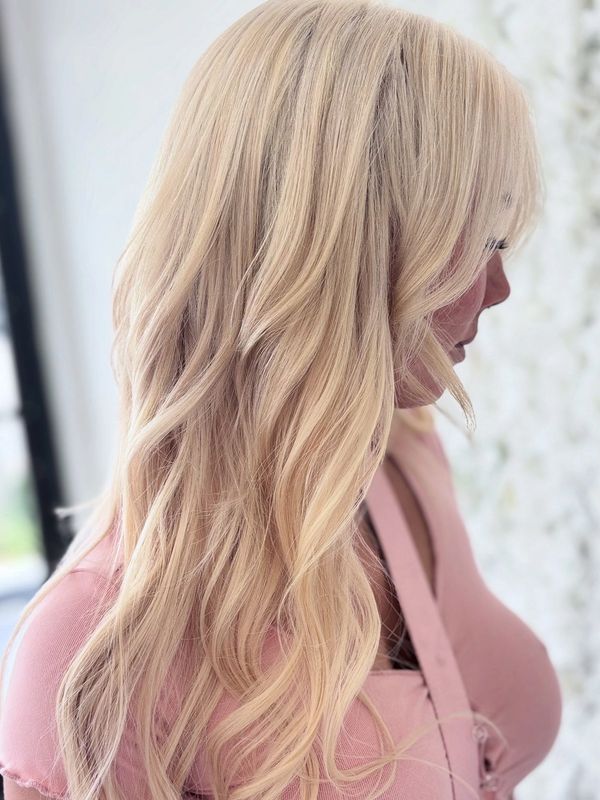 Woman with long, wavy blonde hair wearing a pink top.