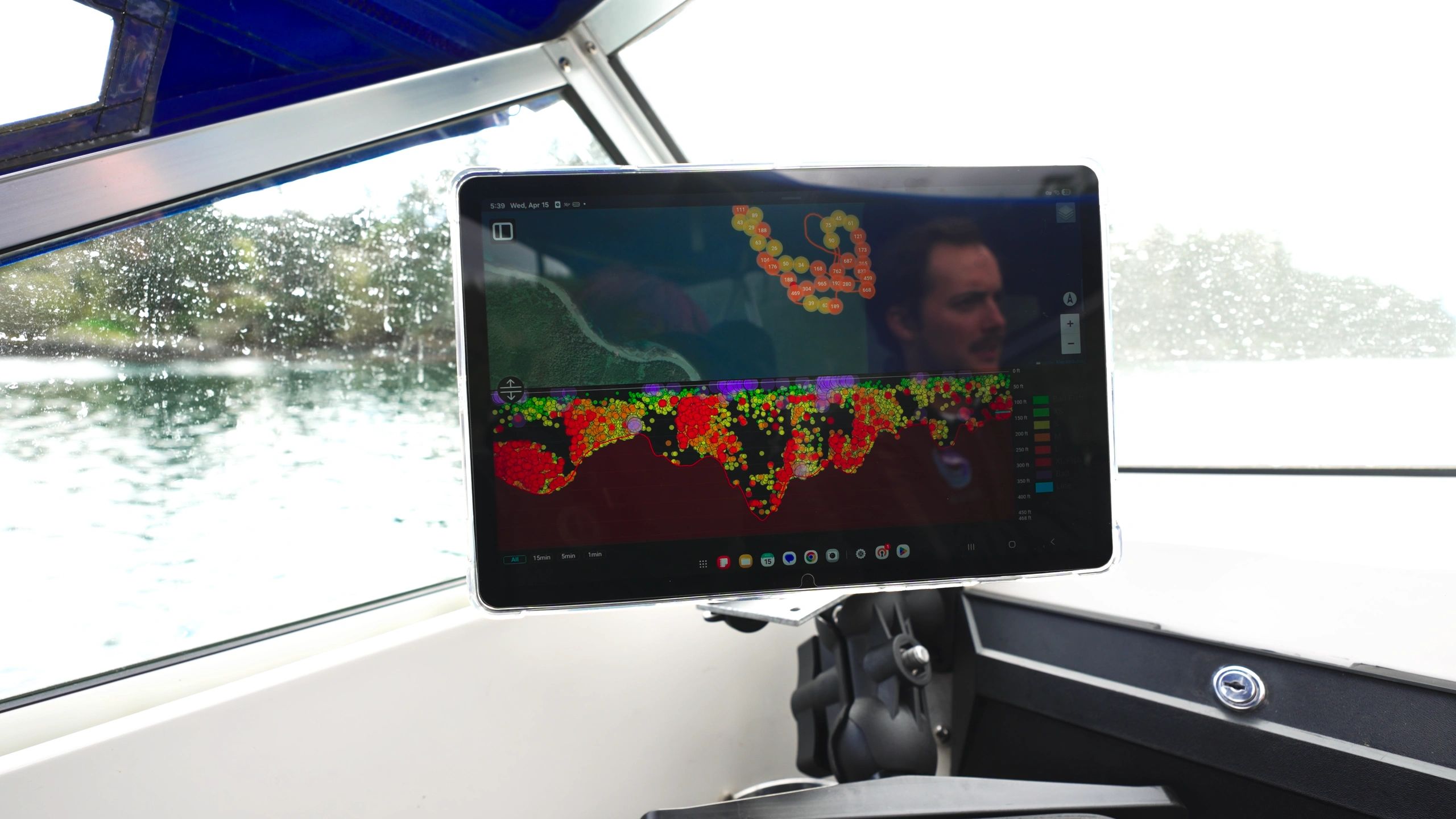 Tablet displaying colorful data map inside a boat cabin with water outside.