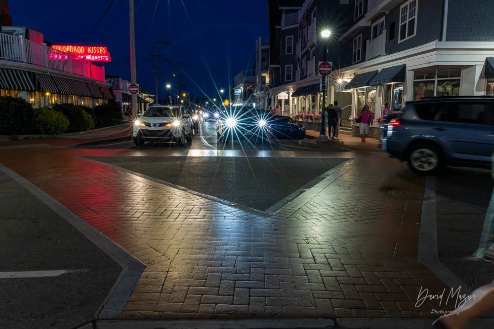 Nighttime street scene with cars and pedestrians under glowing lights.