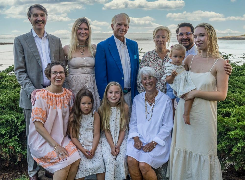 A multi-generational family poses outdoors near water, smiling together.