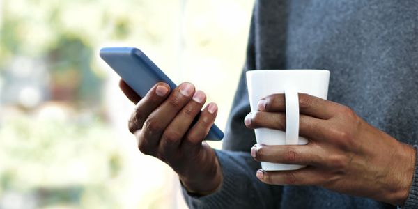 Man in a grey sweater holding a coffee mug looking at his phone