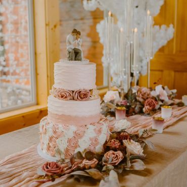 Elegant three-tier wedding cake with rose decorations and topper.