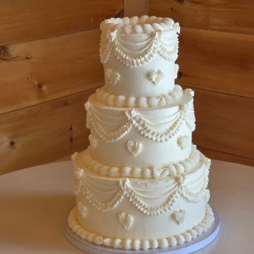 Three-tier white wedding cake with intricate pearl-like icing decorations.