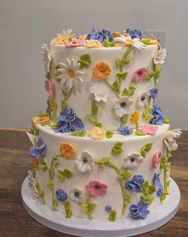 Two-tier cake decorated with colorful edible flowers and green vines.
