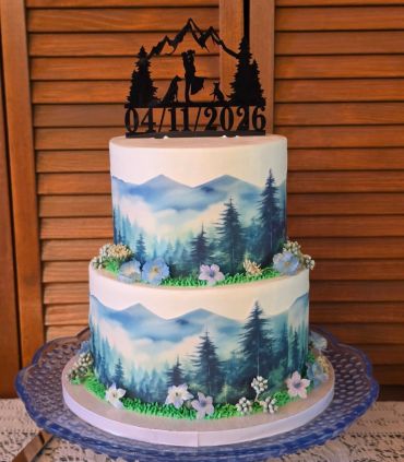 Two-tiered cake with mountain scenery and a romantic topper dated 04/17/2016.