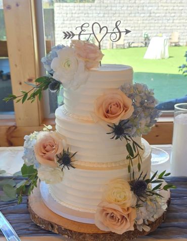 Elegant three-tiered white wedding cake adorned with pastel flowers and initials topper.