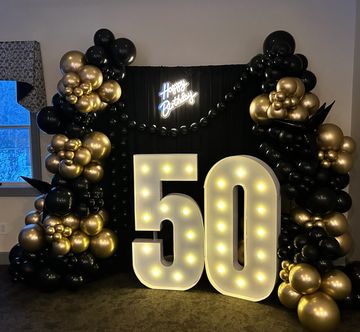 Illuminated '50' with black and gold balloon decorations for a birthday party.
