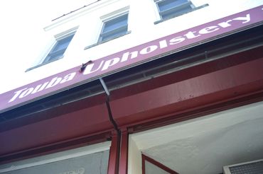Close-up of a building sign reading 'Touba Upholstery' with red and white colors.