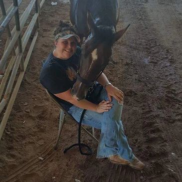 Person sitting with a horse nuzzling their shoulder.