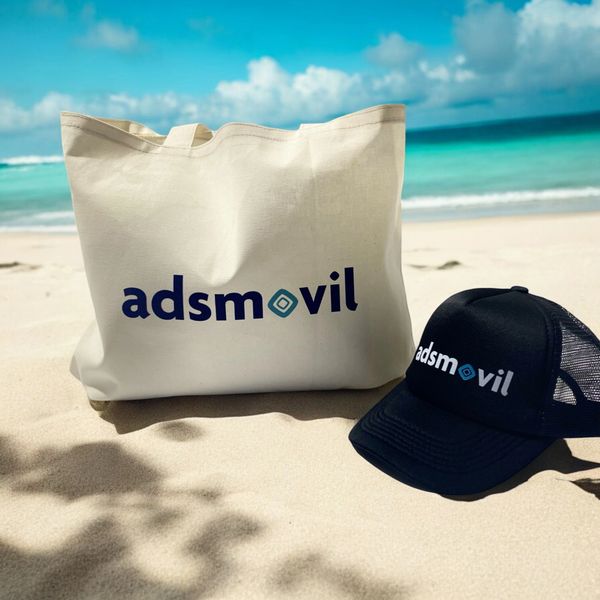 Beach scene with Adsmovil branded tote bag and cap on sand.