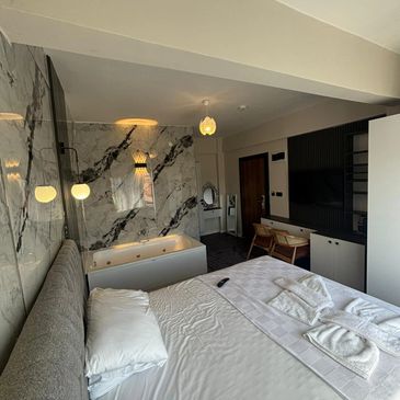 Modern hotel room with a bed and a bathtub separated by a glass wall.