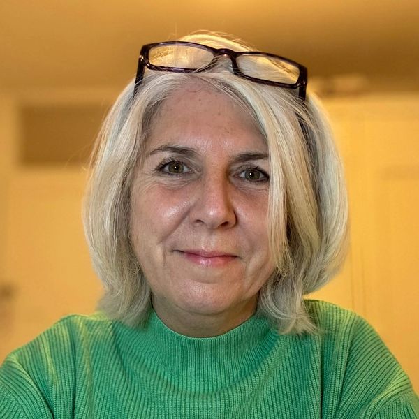 Picture of woman with shoulder length white blond hair wearing a green jumper and with glasses on he